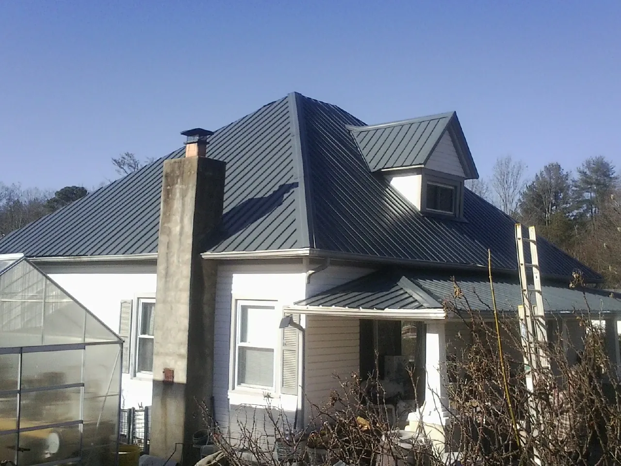 Dark blue standing seam metal roof on a white farmhouse with dormer — Slate & Tile Roof Repair by Roofing Brothers in Frost