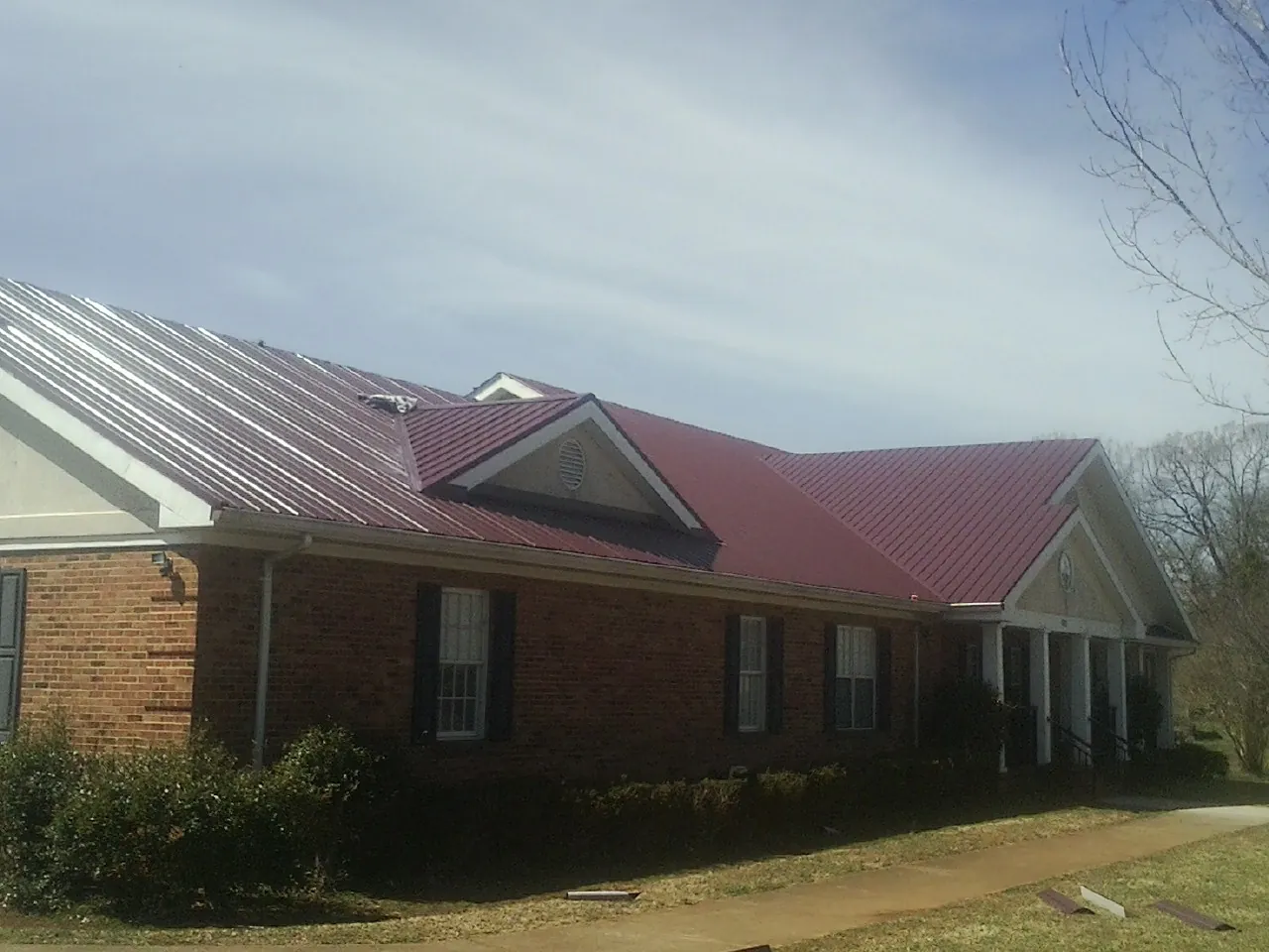 Red metal roof with gabled entries on a long brick building, from a Hail Damage Roof Repair job in Frost