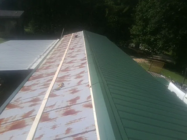 Old rusted panels beside newly installed green metal roofing — Wind Damage Roof Repair by Roofing Brothers in Frost
