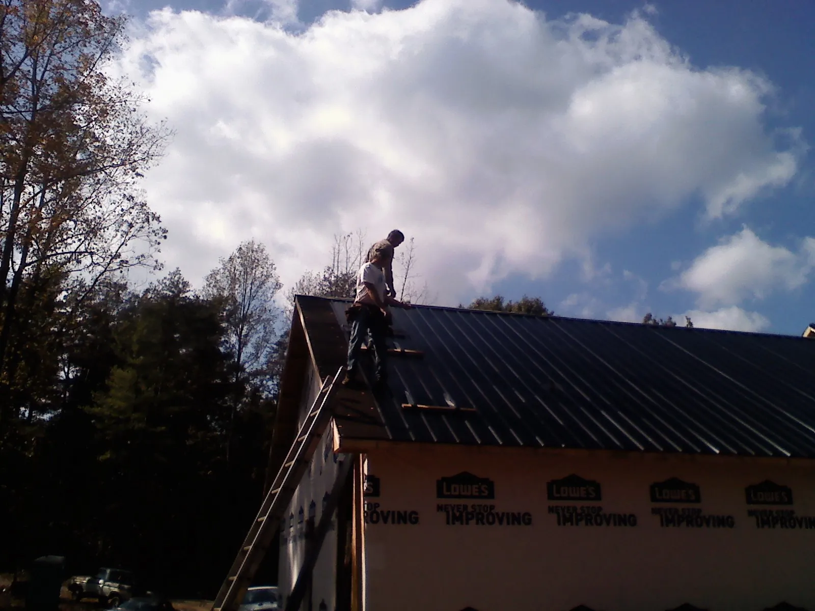 Roofer fastening dark metal panels high against a cloudy sky, from a Roof Inspection job in Frost
