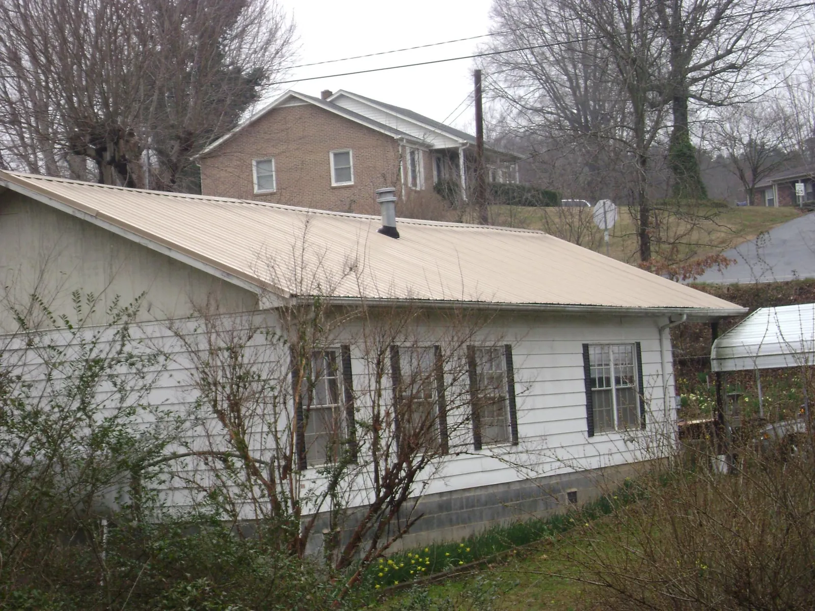 Tan metal roof on a white sided house set into a hillside — Commercial Roofing by Roofing Brothers in Frost