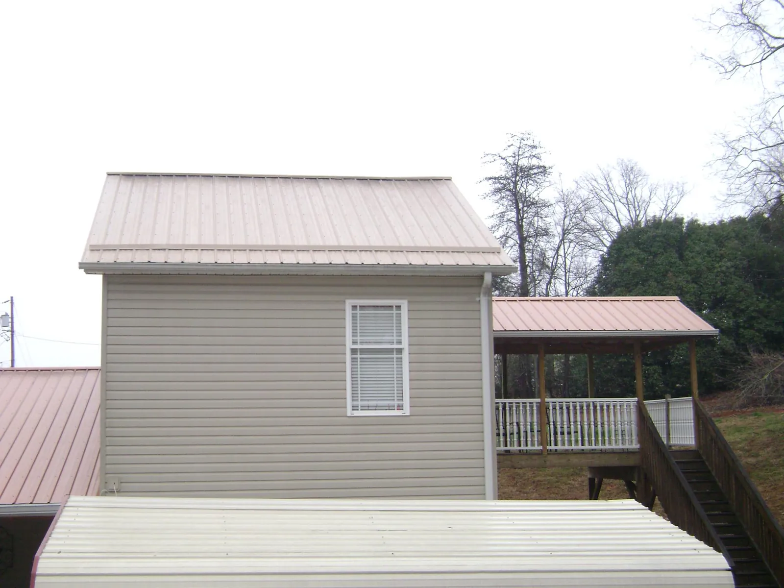 Tan metal roofs on a two story addition and attached porch, from a Roof Replacement job in Frost